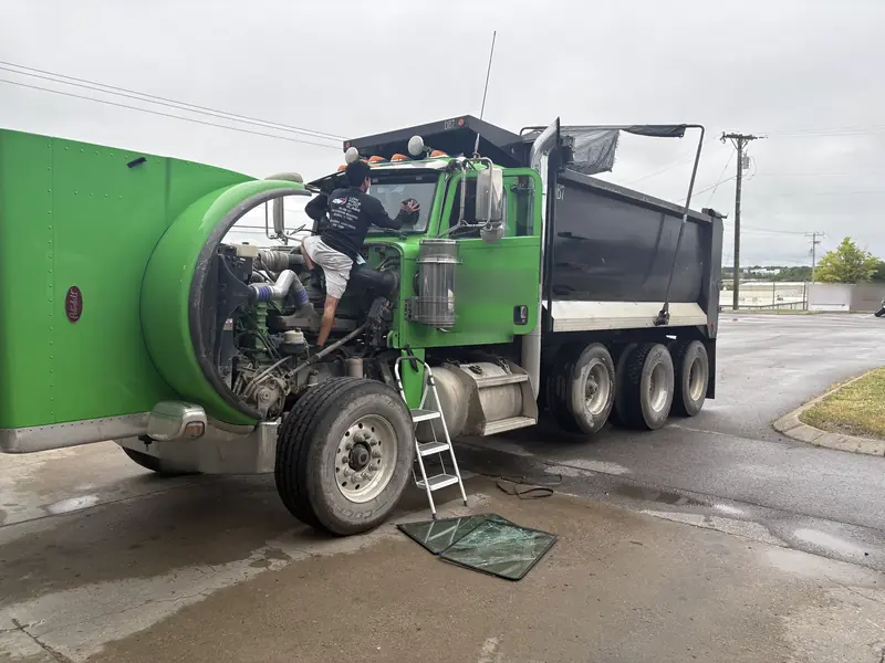 Technician servicing a green dump truck outdoors
