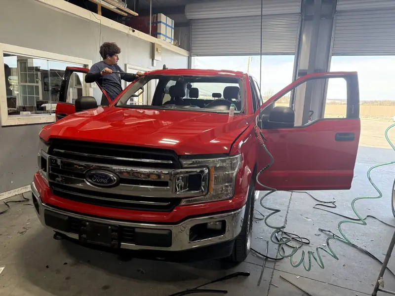 Red Ford F-150 pickup with a technician working at its windshield at our Nashville shop