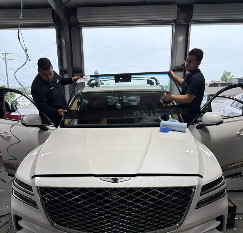 Two Low Price Auto Glass technicians setting a new windshield on a white Genesis SUV at our Nashville shop