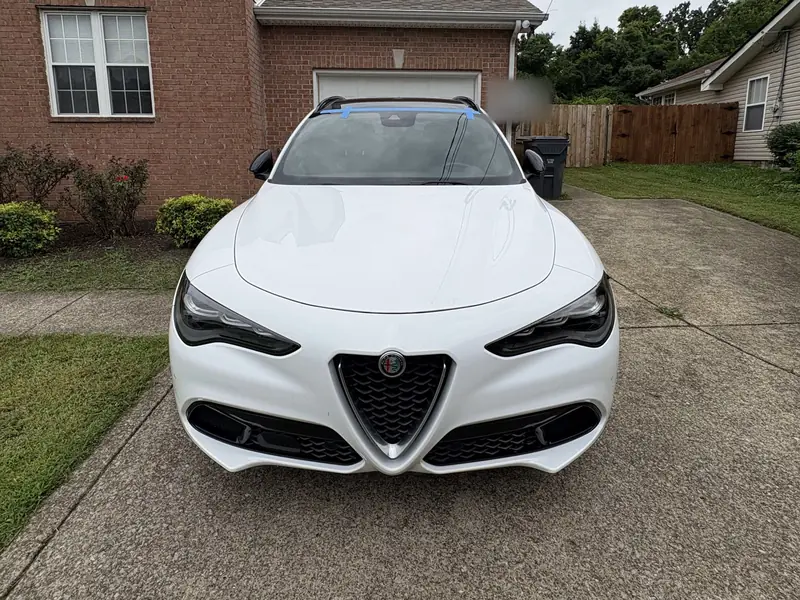White Alfa Romeo with a new windshield, still taped after installation, in a customer's driveway