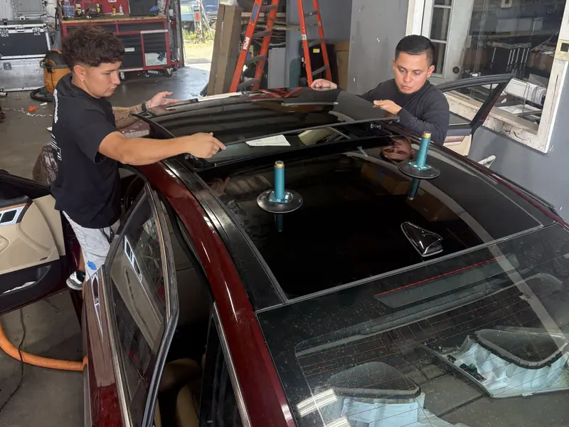 Two technicians lifting a sunroof glass panel off a sedan with suction cups at our Nashville shop