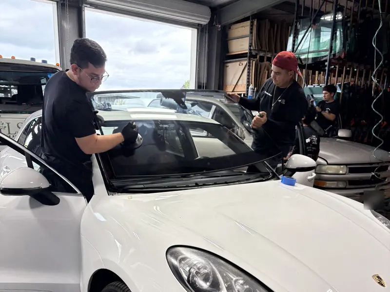 Two Low Price Auto Glass technicians setting a new windshield on a white Porsche Macan at our Nashville shop